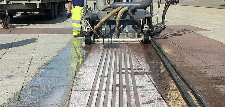 Foto: In eine mit Betonfliesen verlegte Freifläche fräst ein Arbeitsgerät sieben ebenmäßige Rillen.